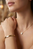 Close-up of a person wearing a gold necklace and bracelet with a blurred background